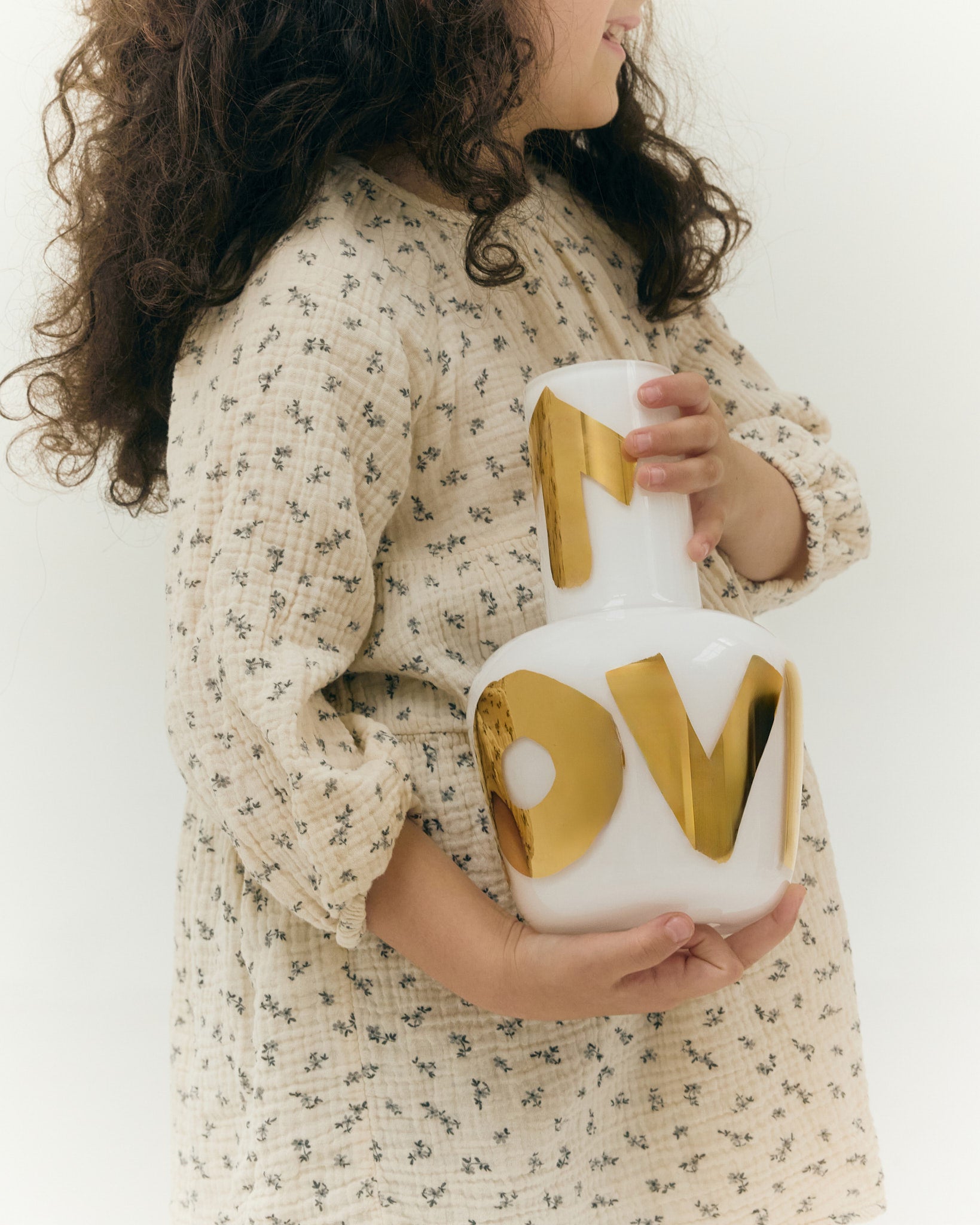 Dívka držící bílou vázu Unnamed s nápisem LOVE v pravém zlatě, součást exkluzivní kolekce Artisème x QUBUS.